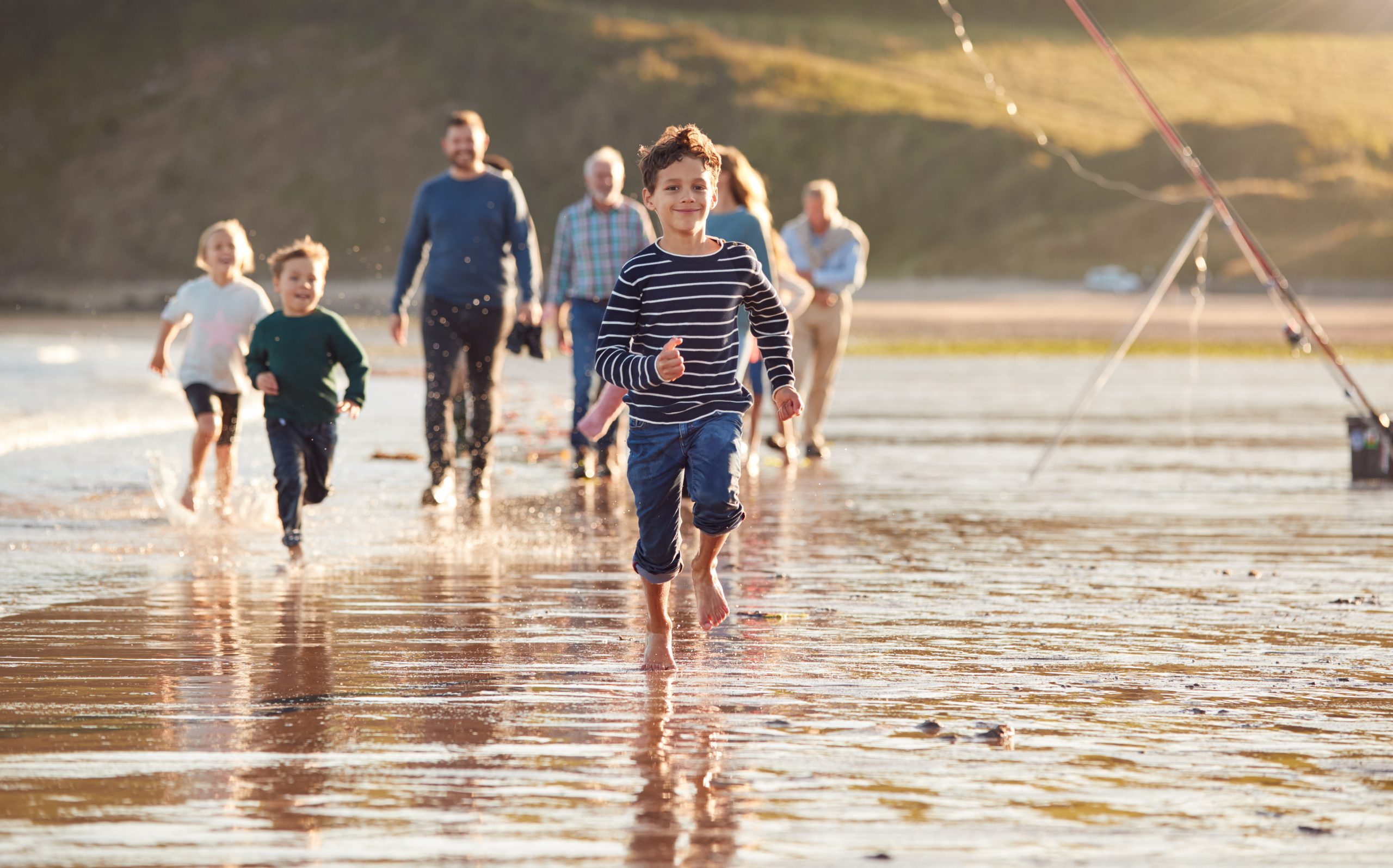 Children Run Ahead As Multi-Generation Family Walk Along Shore On Winter Beach Vacation